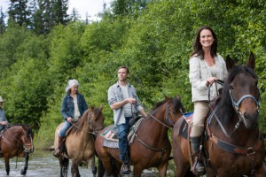 Group of four horse riders crossing river.